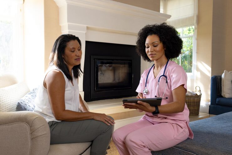Services mature biracial woman sitting with young biracial healthcare worker holding tablet home 13339 363174
